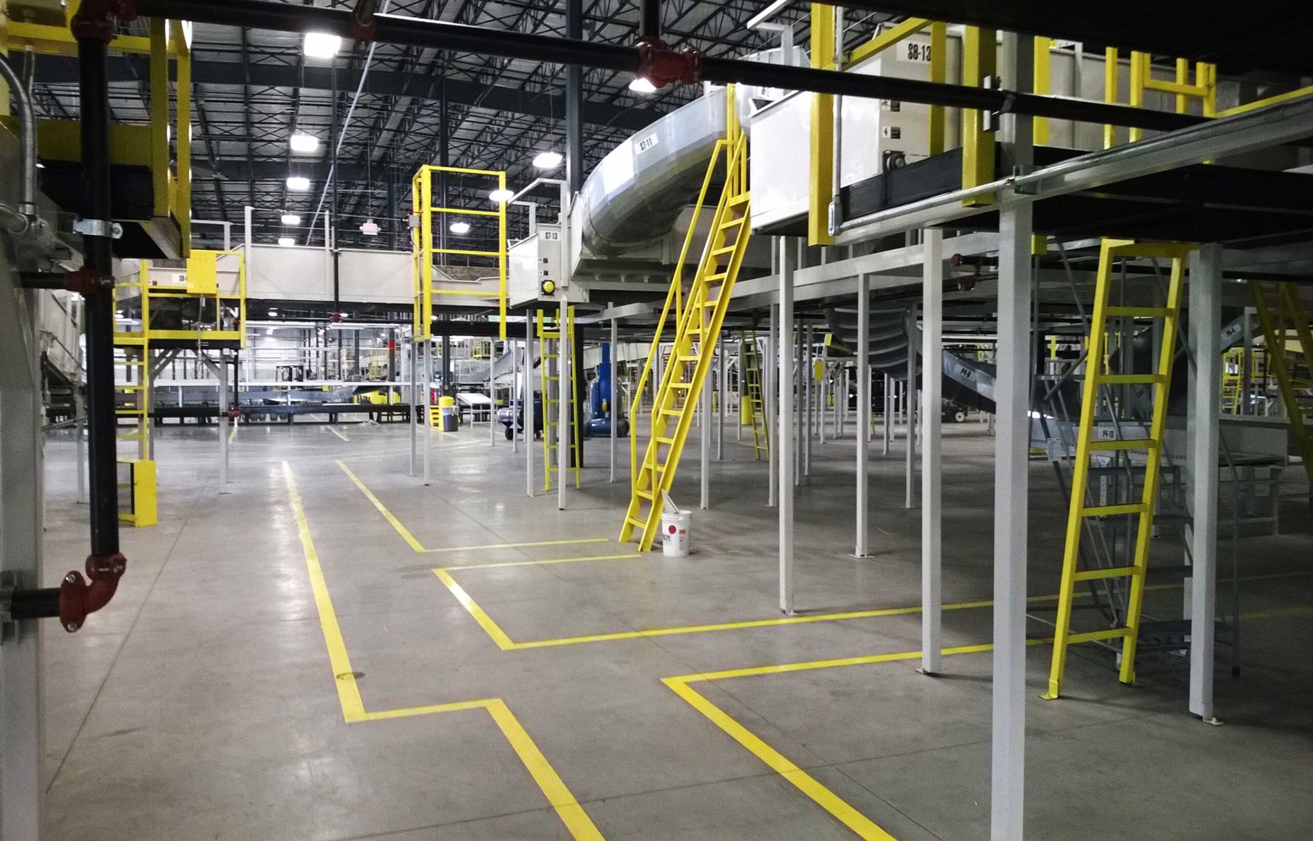 Distribution center showcasing conveyor belts, machinery, and yellow ladders.