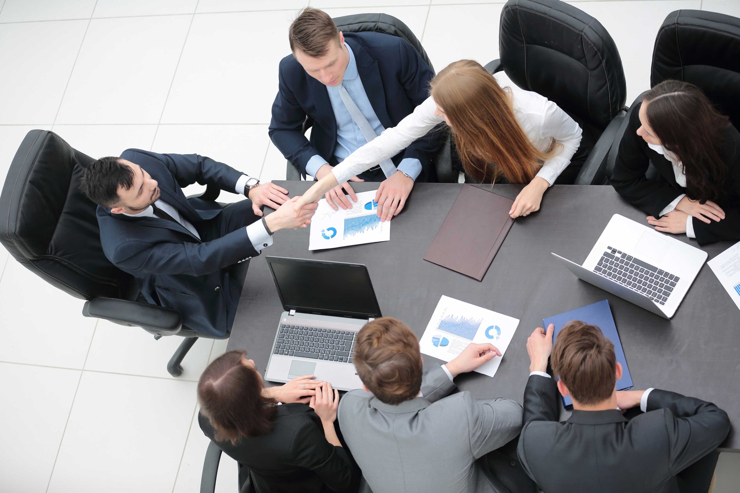 Group of male and female partners discussing government initiatives in a conference room while taking notes on their laptops.