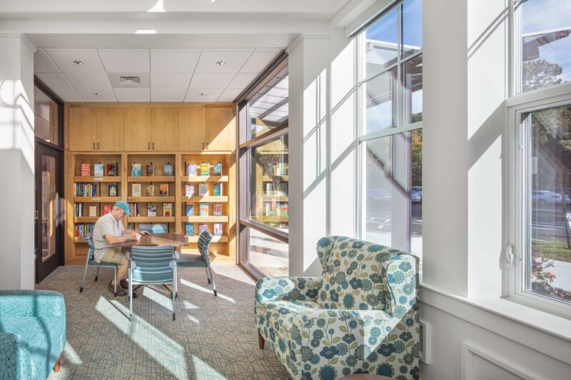Senior citizen reading a book in a well lit room in the Hadley Senior Center library.