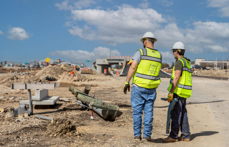 Two workers wearing personal protective equipment evaluating the land for surveying.