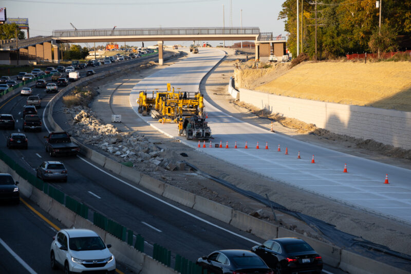 Cars driving on the highway alongside roadway construction and traffic cones.