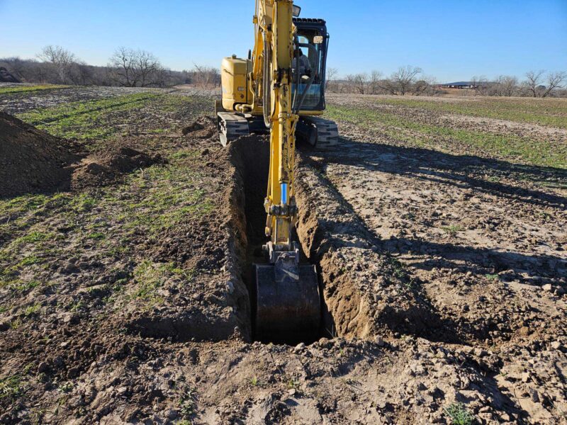 Yellow bulldozer creating a trench in the ground.