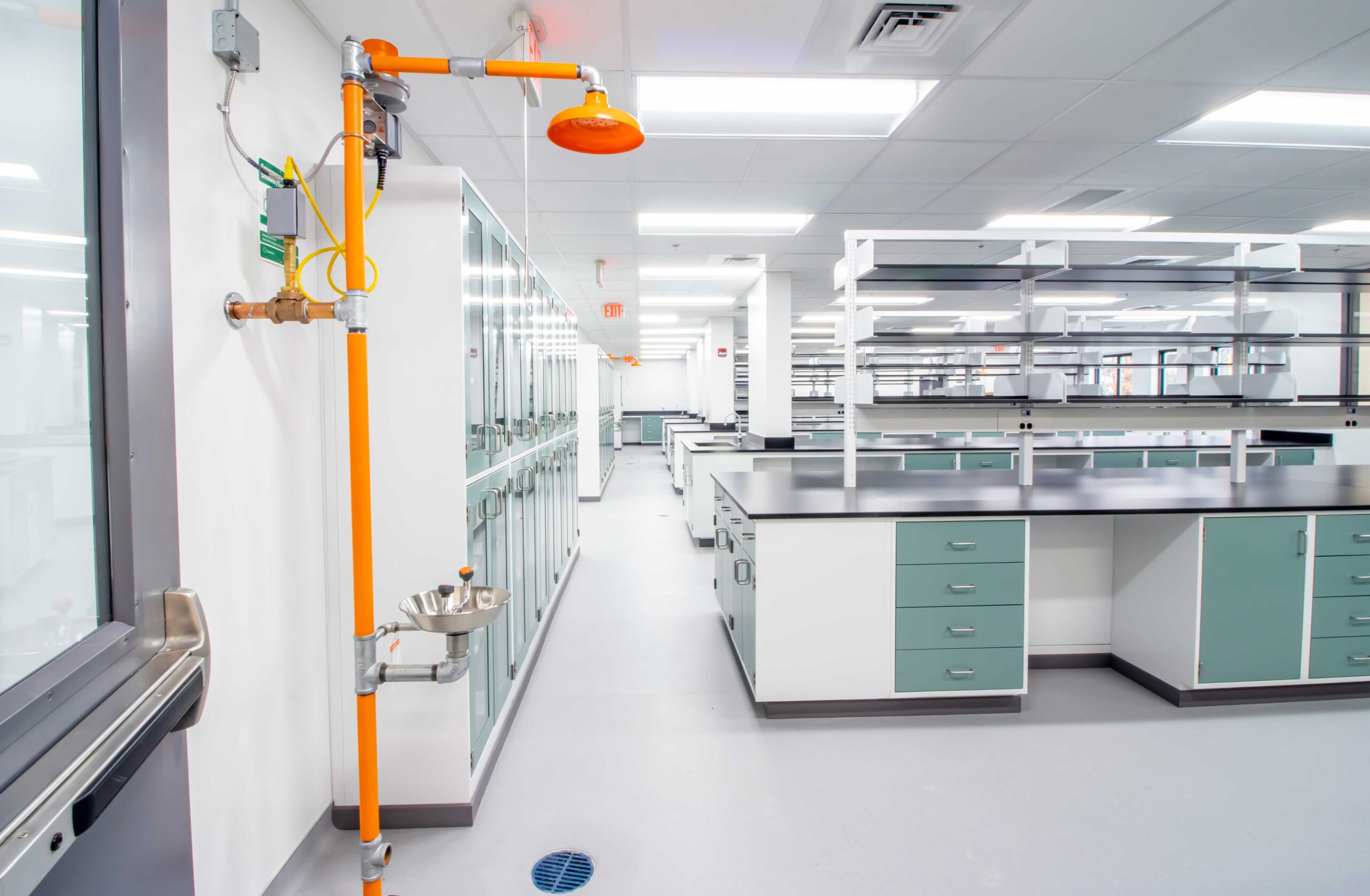 Research lab featuring a bright orange emergency shower, lab desks for testing, and LED ceiling lights.